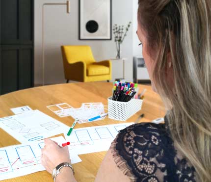 Joanne Hughes sat at a table using pens and paper to draw the initial website framework